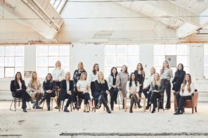 21 kvinnor står och sitter i en ljus fabrikslokal