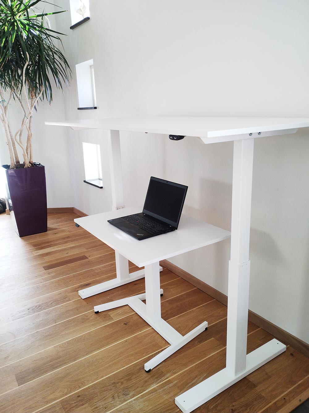 Ett lågt skrivbord står under ett mycket högre skrivbord mot en vit vägg.