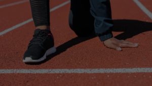 Närbild på en löpares fötter och händer i startposition på en löparbana.