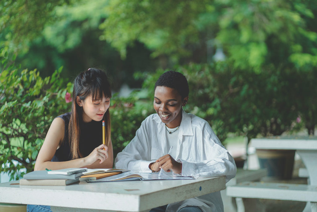 Två studenter sitter vid ett bord utomhus och studerar.