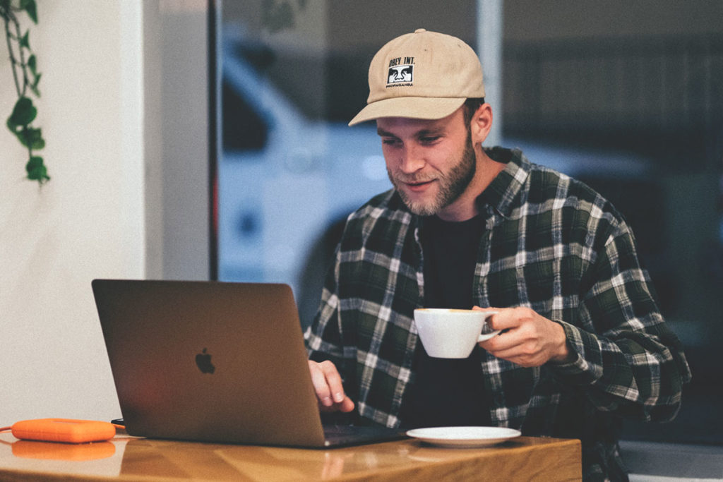 En student sitter på ett café, dricker kaffe och jobbar på sin laptop.