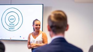 En entreprenör står framför en publik. På väggen bakom henne sitter en skärm som visar en bild av modellen The Golden Circle.