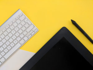 En trådlöst tangentbord, en ipad och en penna ligger på ett gult bord.