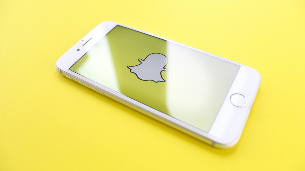 En telefon med snapchat-spöket på skärmen. Bakgrunden är gul.