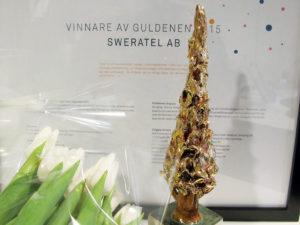 En bild som visar statyetten Guldenen framför en tavla med diplomet för årets vinnare. företaget Sweratel.