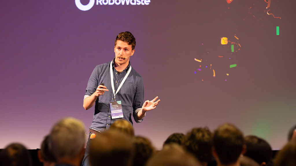 Philip Alm som driver företaget Norditech i Jönköping föreläser på AI-dagen 2023. Han står på en scen med lila bakgrund och i förgrunden syns huvuden på människor i publiken.