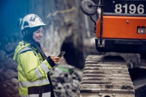 Ett foto på en kvinna vid en byggarbetsplats som håller i en mobiltelefon