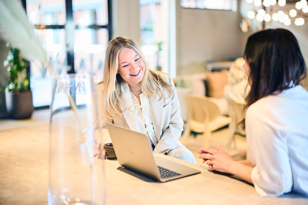 Två studenter sitter vid ett bord. De dricker kaffe och tittar på en dator.