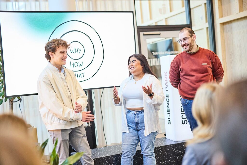 Tv&aring; m&auml;n och en kvinna st&aring;r framf&ouml;r en sk&auml;rm d&auml;r modellen "The Golden Circle syns". Personerna ser glada ut och ser ut att vara mitt i en presentation.