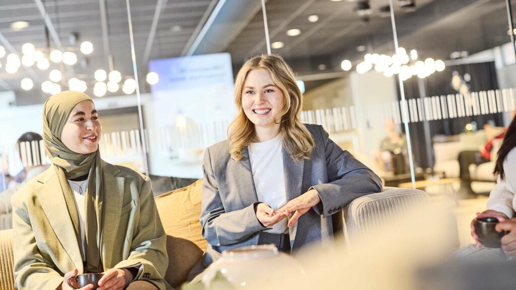 Två personer sitter i en coworking och samtalar. De är glada. 