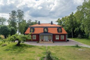 Ett foto som visar ett trähus av fabrikatet Rörvikshus. Huset är rött och omgivet av en lummig trädgård.