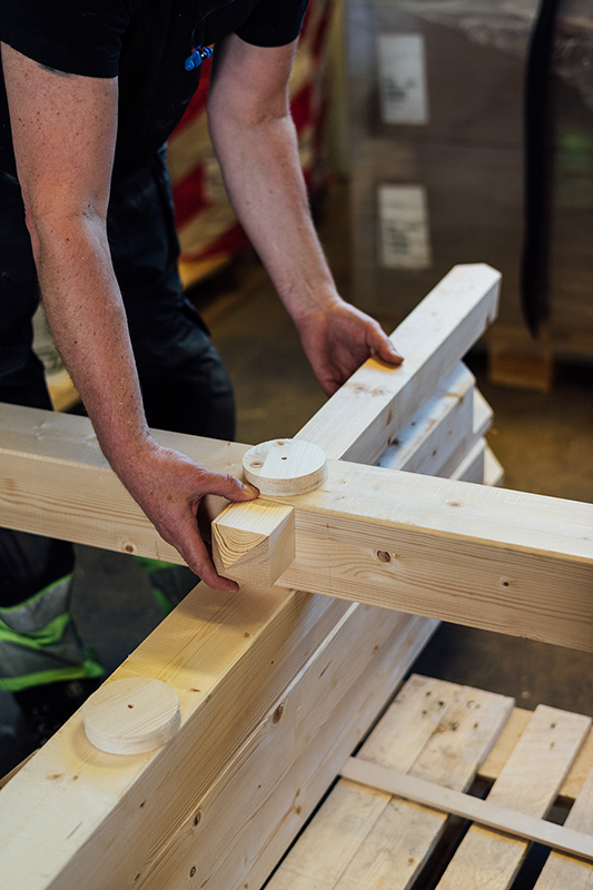 En person arbetar med en träkonstruktion till ett hus i en fabrik.