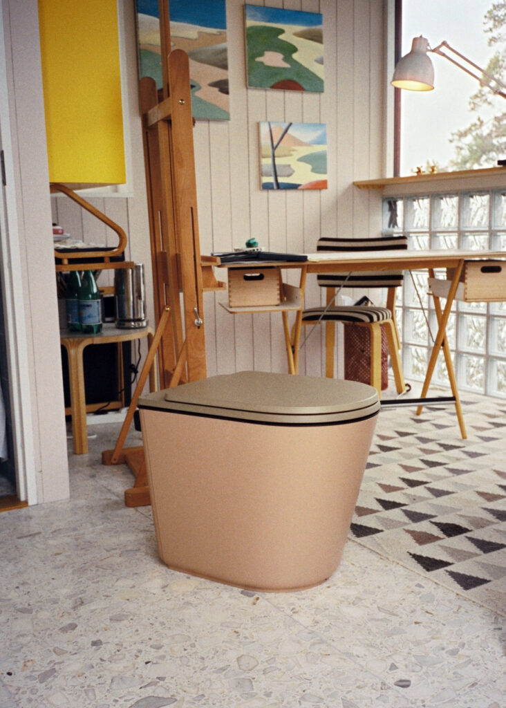 En toalett från Harvest Moon står i ett ljust, kreativt arbetsrum med konstverk, ritbord och staffli.