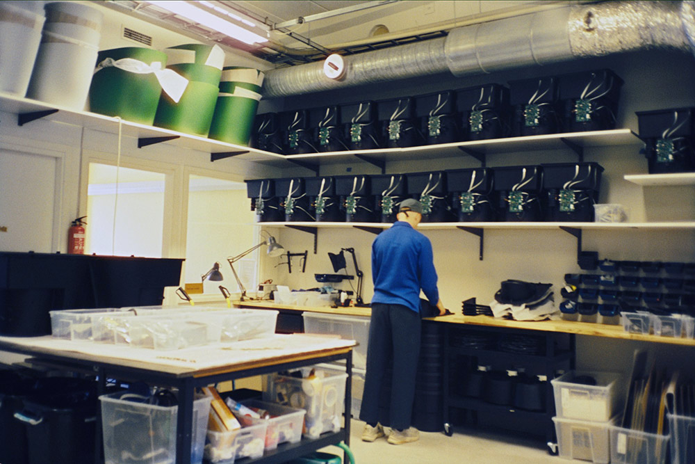 En person arbetar i Harvest Moons verkstad med hyllor fyllda av komponenter och färdiga toaletter.